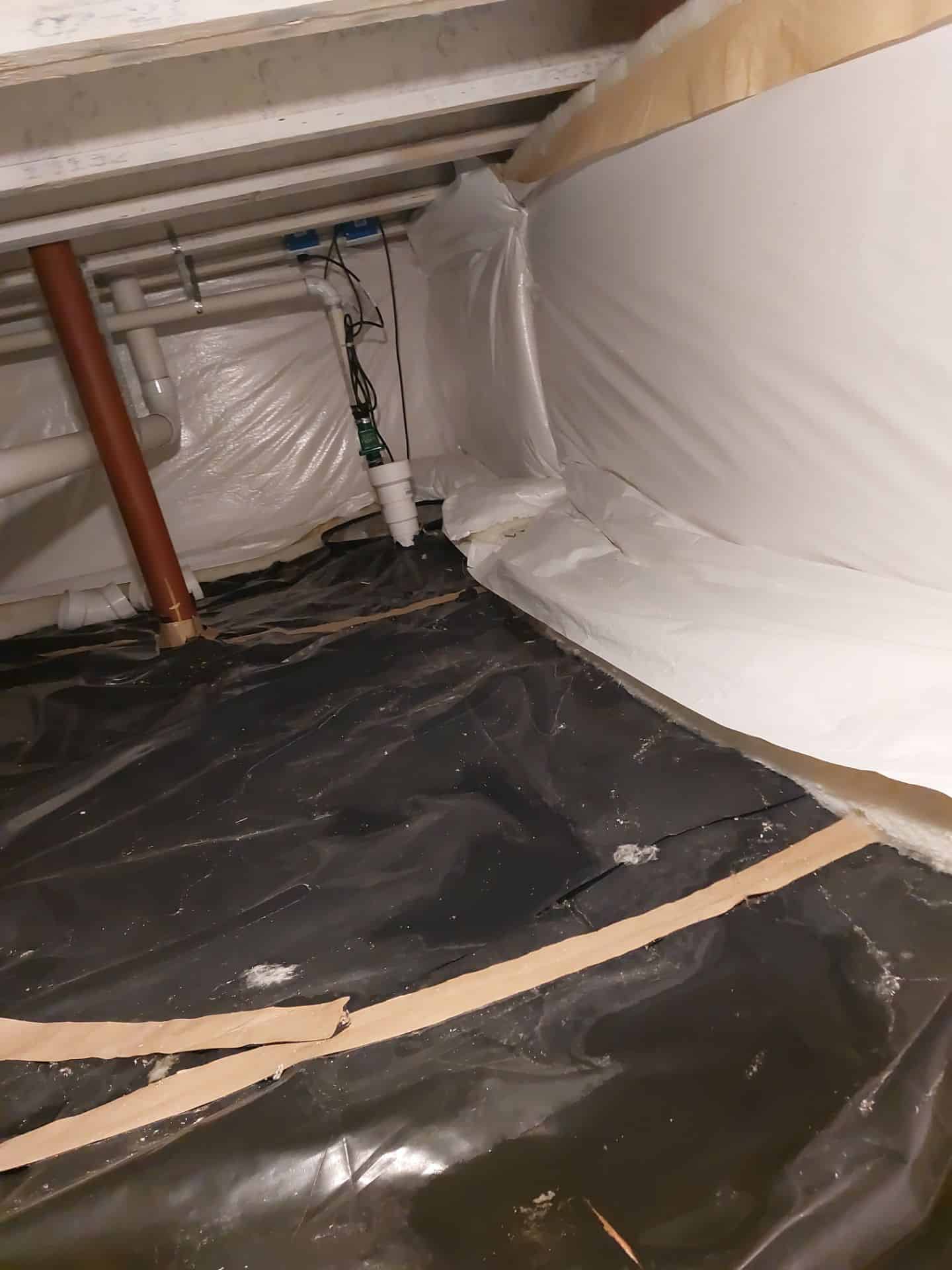 Crawl space with plastic vapor barrier and plumbing system.