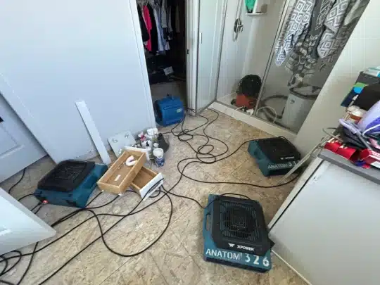Multiple industrial air dryers and cables are spread across a tiled bathroom and closet area during water damage restoration