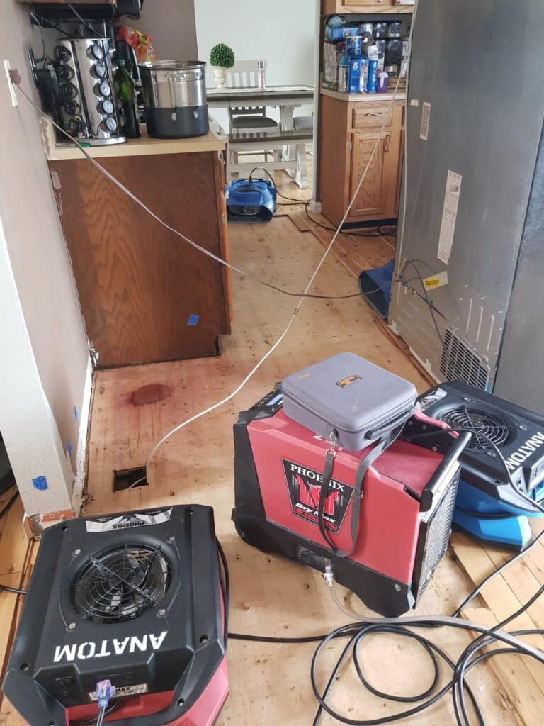 Kitchen undergoing water damage restoration with drying equipment, exposed flooring, and dehumidifiers in use