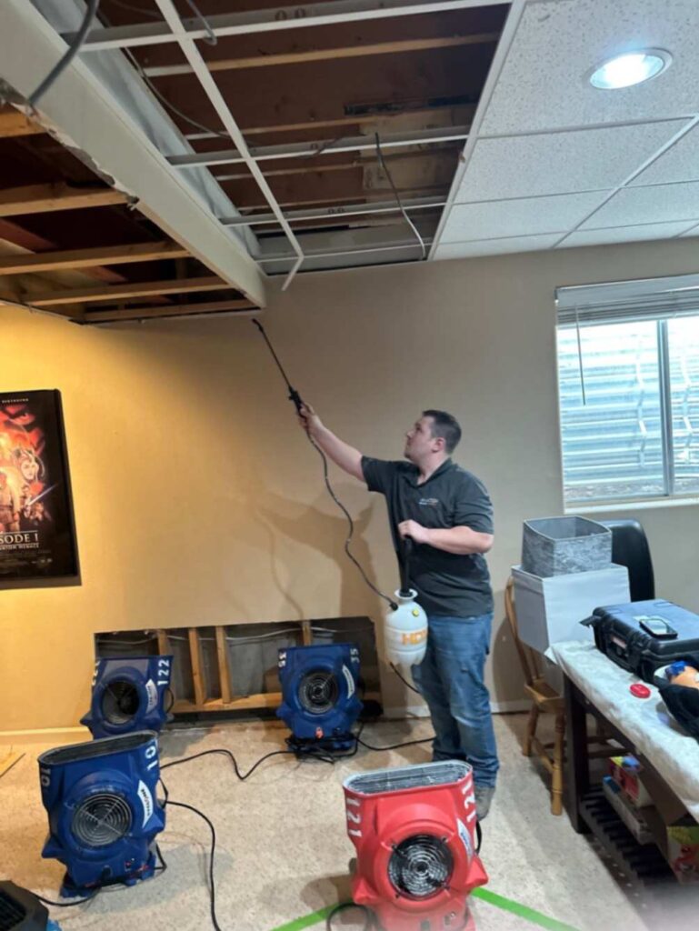 Water damage restoration in progress – Technician treating a ceiling after a severe leak, with industrial air movers drying the space.