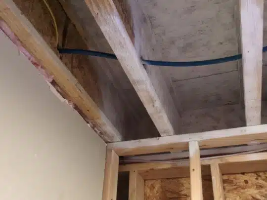 Exposed ceiling beams and framing with visible plumbing lines during a home restoration project.