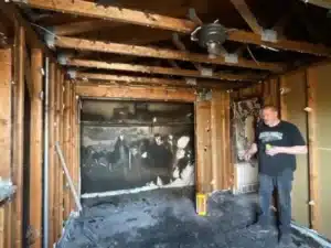 person is standing in a fire-damaged room. The walls are covered in soot.