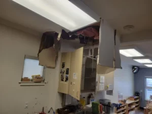 An interior view of a room with a severely damaged ceiling, exposing insulation and hanging debris.
