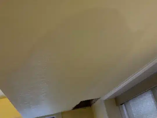 A ceiling with visible water damage and a hole near a window