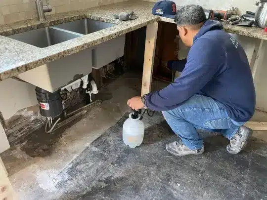 A person working under a kitchen sink during restoration