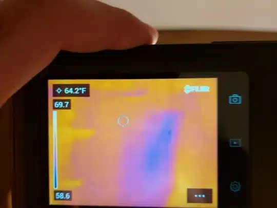 A person holding a thermal imaging camera displaying a heat map in a basement with concrete walls