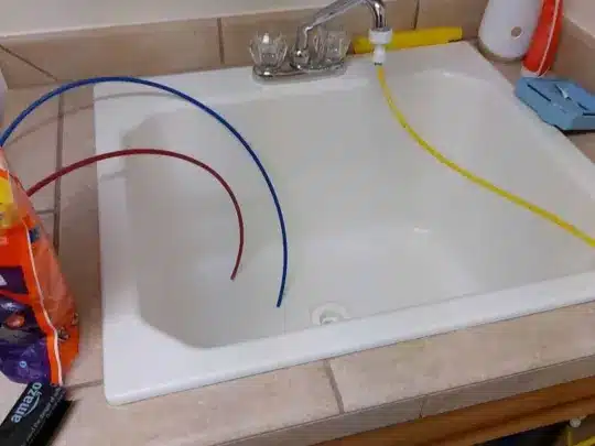 A kitchen sink with colored pipes and cleaning supplies on the counter
