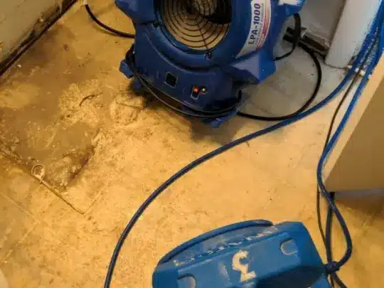 Two air movers positioned on a damaged floor, with cables connected, in an indoor setting