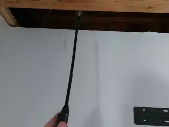 A person holding a tool with a long probe against a ceiling with exposed wooden beams near a wall