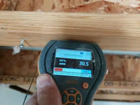 A person holding a moisture meter against a wooden ceiling with exposed beams, displaying a reading of 30.5