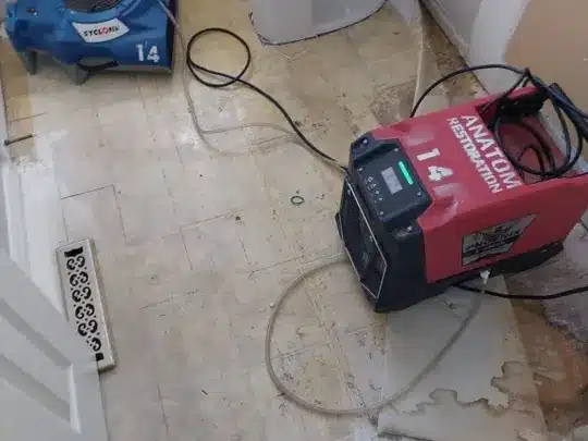 A blue drying machine and a red drying machine with cables, positioned on a damaged wooden floor near a door
