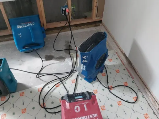 A person standing near a red drying machine and two blue drying machines on a floor, with exposed walls and cables, in a room