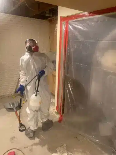 Worker in full PPE spraying inside sealed area.
