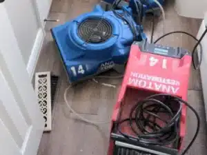 A blue and a red drying machine on a wooden floor, connected by cables, positioned near a door in a room