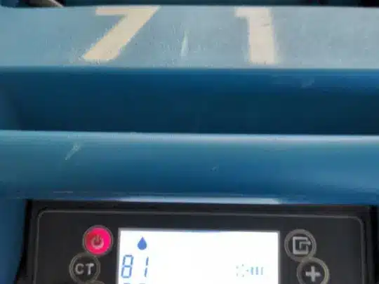A close-up view of a blue drying machine's control panel, displaying temperature and humidity readings