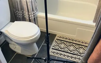 A bathroom with a white toilet, bathtub, diamond-patterned rug, and a black pedestal sink, with a striped shower curtain and hanging towel