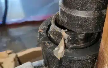 A close-up of a black drain pipe under a sink, surrounded by dust and construction debris, with white tape on the pipe