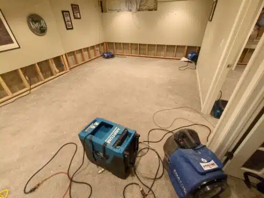 A carpeted room with flood cuts on the lower drywall, where drying equipment is positioned throughout to address water damage.