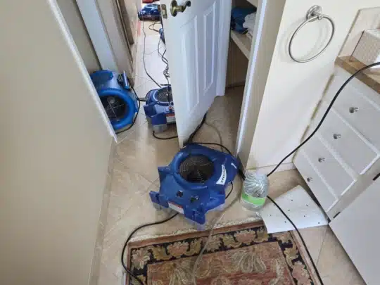 Restoration equipment with multiple air movers drying a hallway and bathroom area