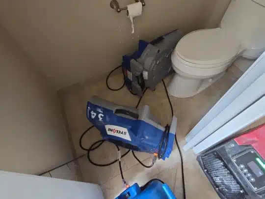 Restoration equipment with air movers positioned inside a bathroom near a toilet