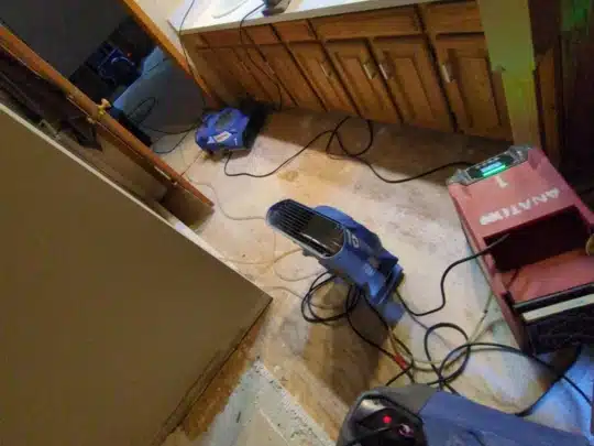 Drying equipment including air movers and a red dehumidifier set up across a bathroom and hallway with exposed flooring