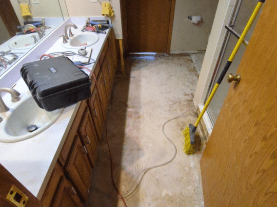Bathroom under restoration with floor stripped down and cleaning tools visible