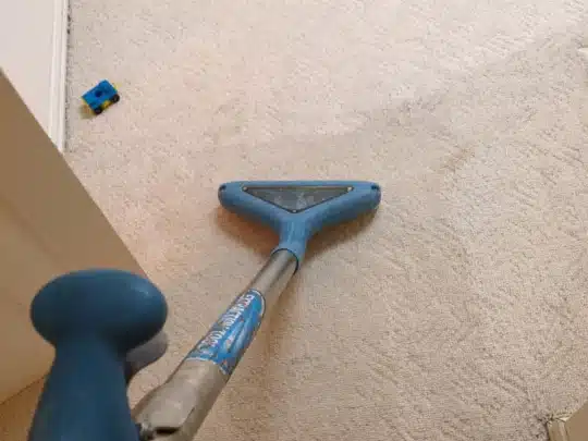 Carpet cleaning wand being used on light-colored carpet with visible water stains