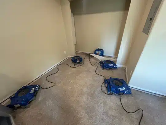 Four air movers placed on carpeted floor in an empty room to dry water damage
