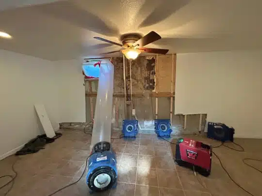 Restoration fans and drying equipment directed at a wall with removed drywall in a tiled room