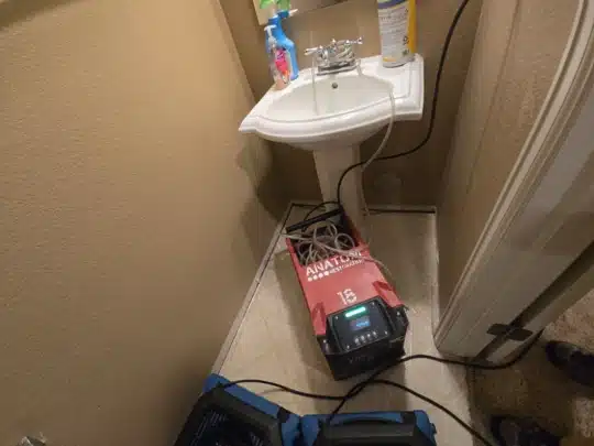 Restoration equipment placed under a bathroom sink with cleaning supplies nearby