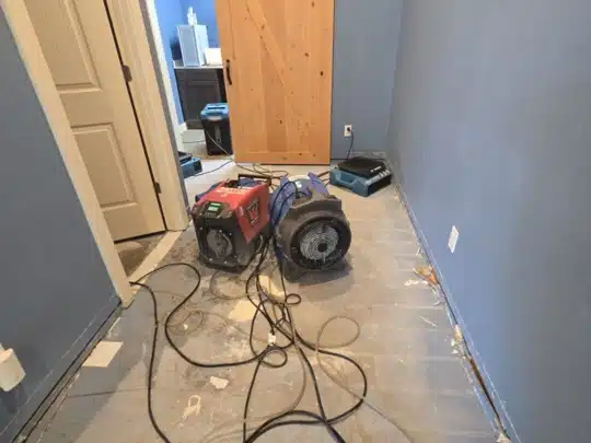 Two drying machines placed on a bare subfloor in a hallway during restoration work.