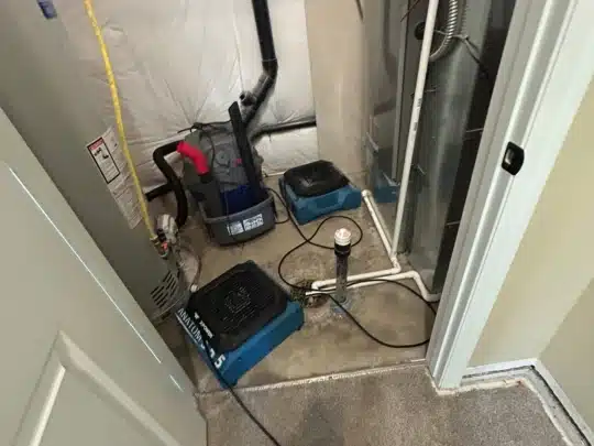 Restoration equipment including air movers and a vacuum placed on a wet concrete floor near a water heater and furnace