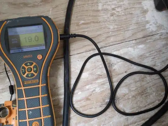 Close-up of a moisture meter placed on wooden flooring, showing a reading of 19.0 percent moisture content