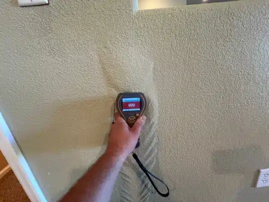 A technician using a moisture meter on a wall to measure water damage