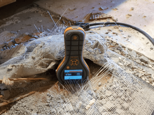 Moisture meter device placed on a damaged concrete floor with mesh and debris