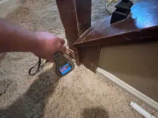 Technician using a handheld moisture meter on carpet and wooden stairs inside a home