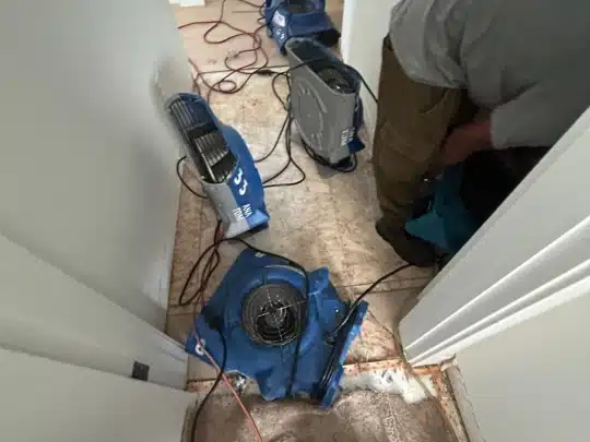 Several industrial air movers and drying machines positioned in a hallway with exposed flooring