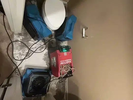 Water damage restoration equipment placed in a small bathroom with a toilet and exposed flooring